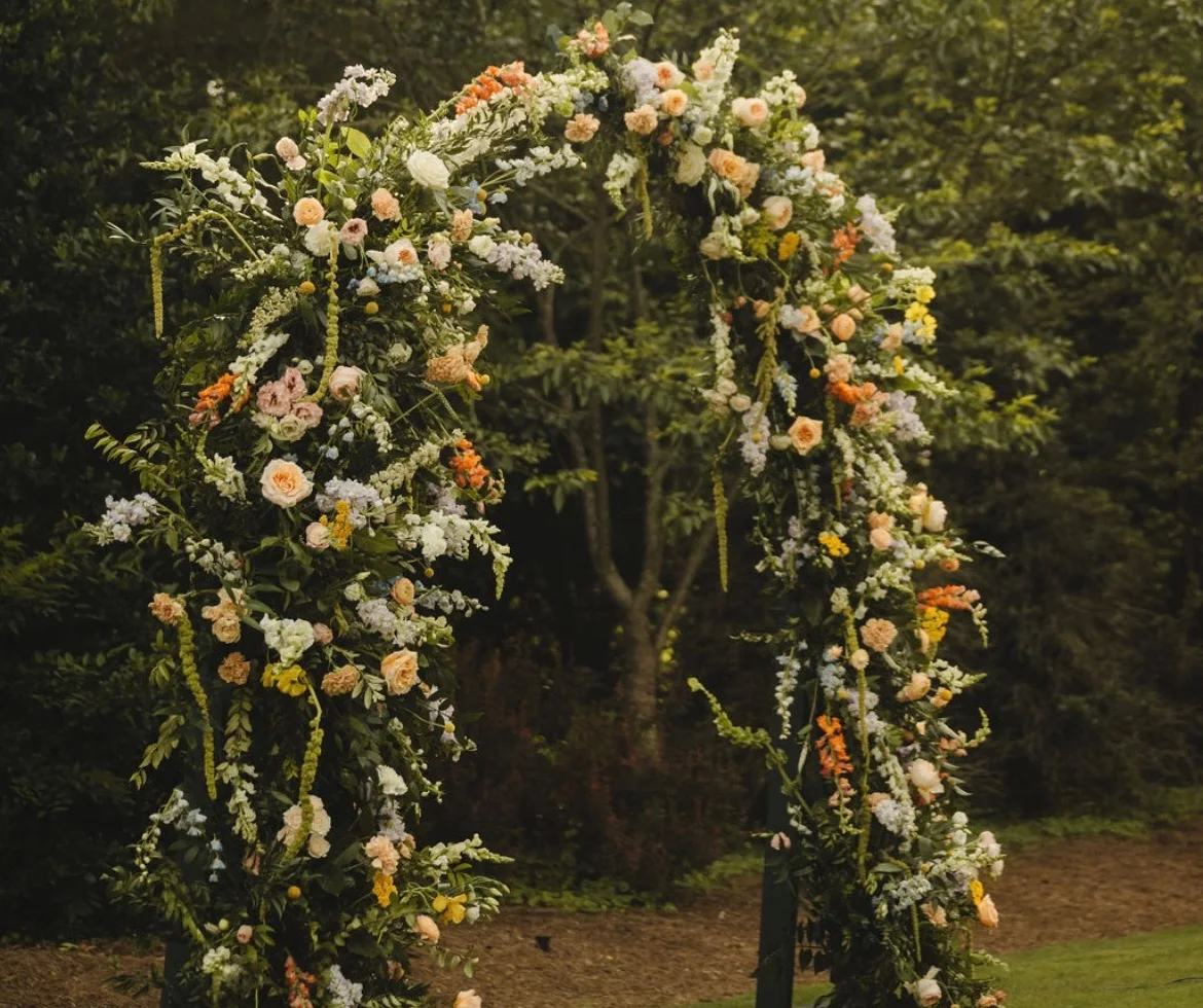 A floral arch with peach and white blooms in the woods