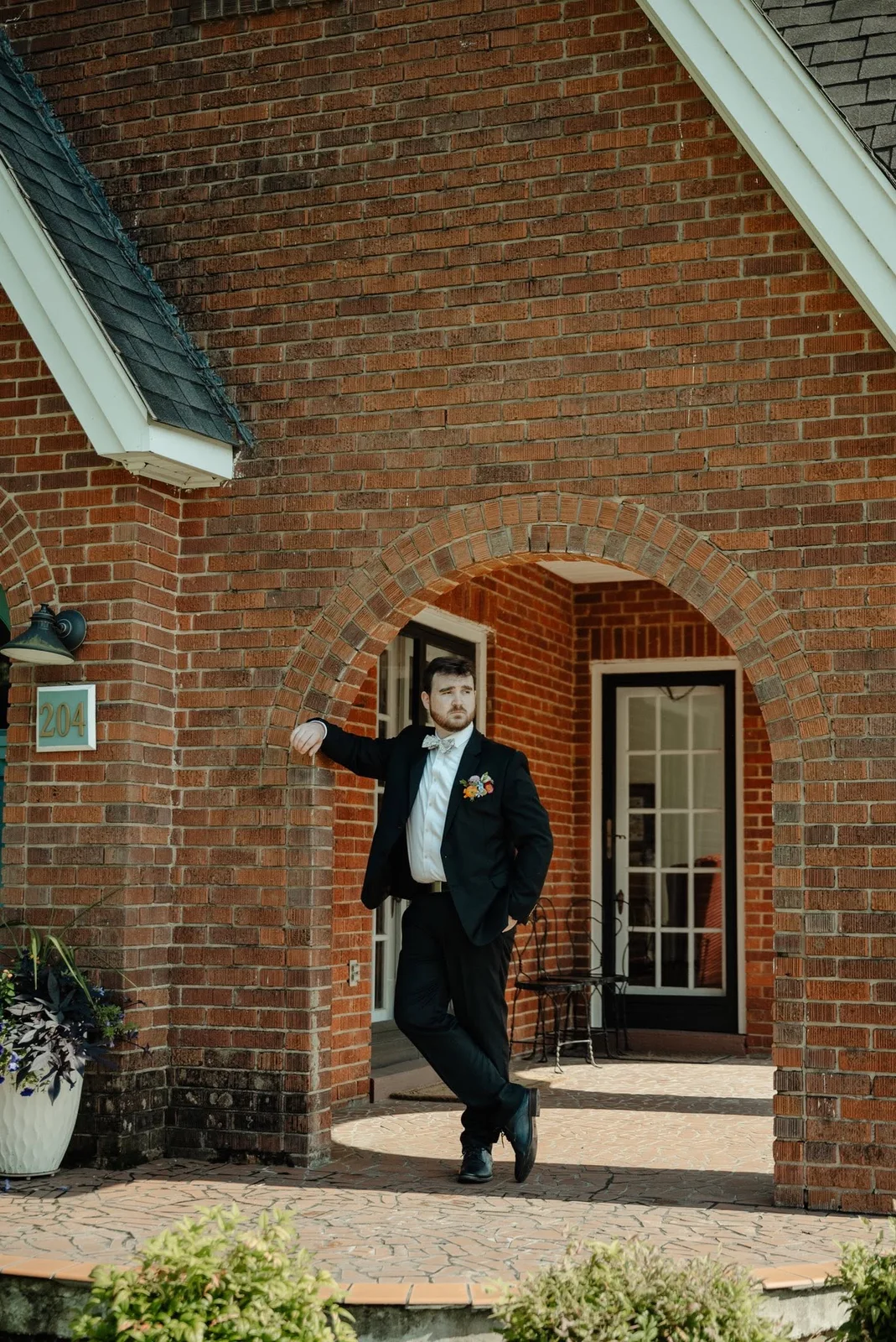 A groom leaning in a brick archway