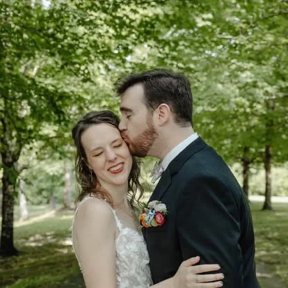 A groom kissing his bride on the forehead in the woods