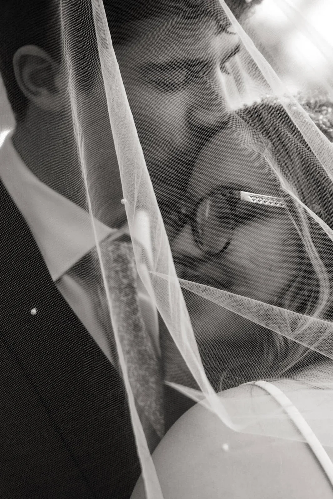 A groom kissing his bride beneath her veil, in black and white